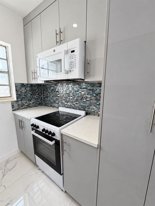 Modern kitchen featuring gloss-finish cabinetry, stone-style countertops, mosaic tile backsplash, stainless steel hardware, and large-format tile flooring