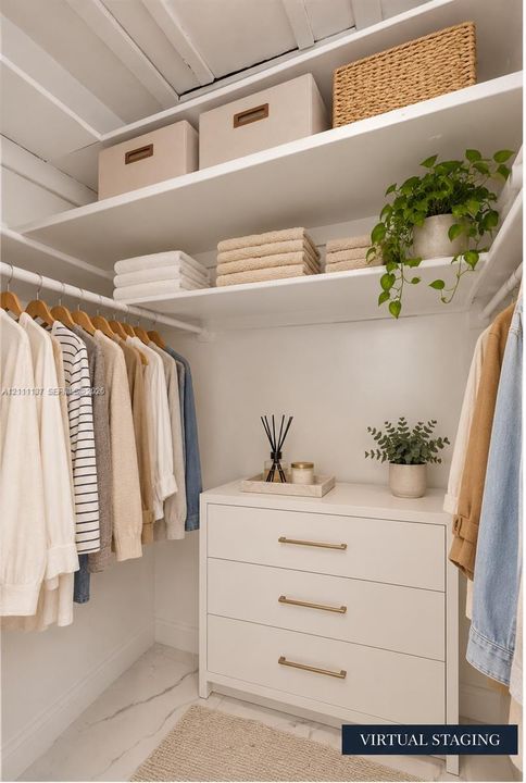 Walk-in closet featuring tiered white shelving, a built-in three-drawer dresser with metallic hardware, and white stone-finish flooring