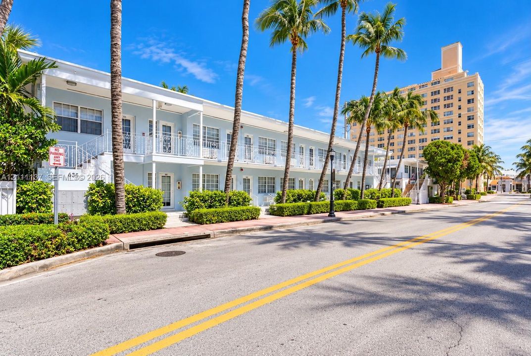 Two-story exterior featuring light-toned masonry, wrought iron railings, private balconies, and manicured perimeter landscaping with palm trees