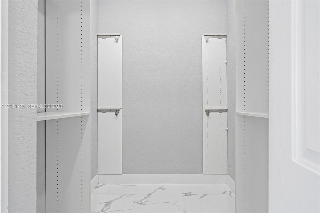 Storage space featuring white built-in shelving units, adjustable support tracks, and white stone-patterned flooring
