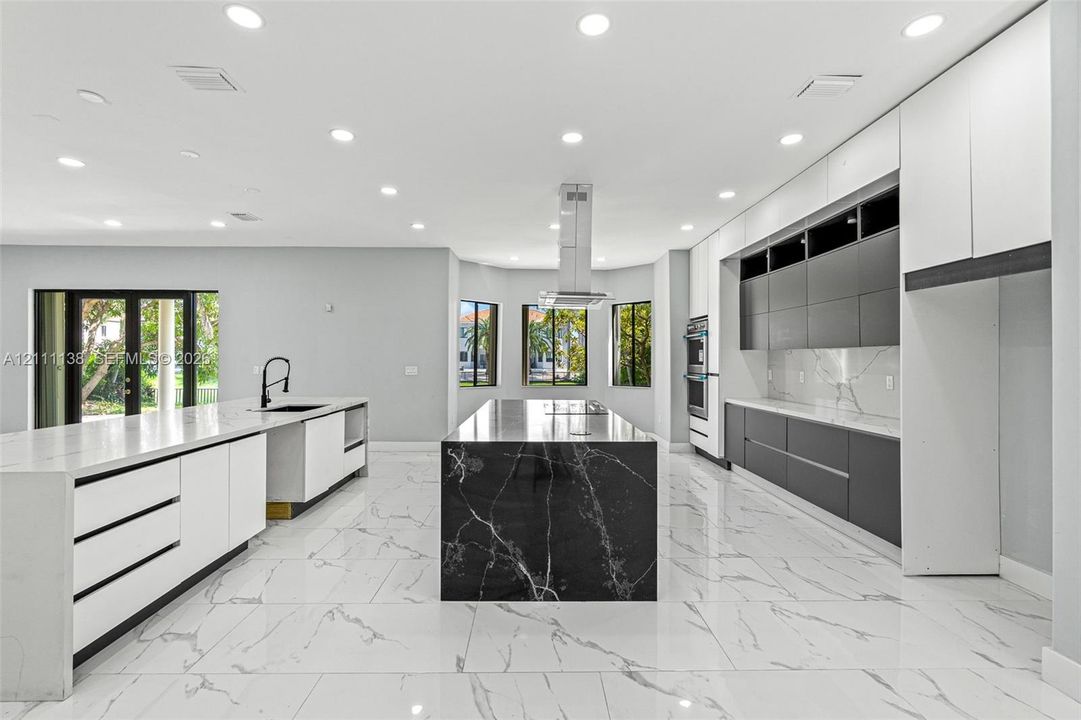 Modern kitchen featuring flat-panel cabinetry, a central island with a contrasting stone finish, stone-surface countertops, tile flooring, and a stainless steel ceiling-mounted vent hood
