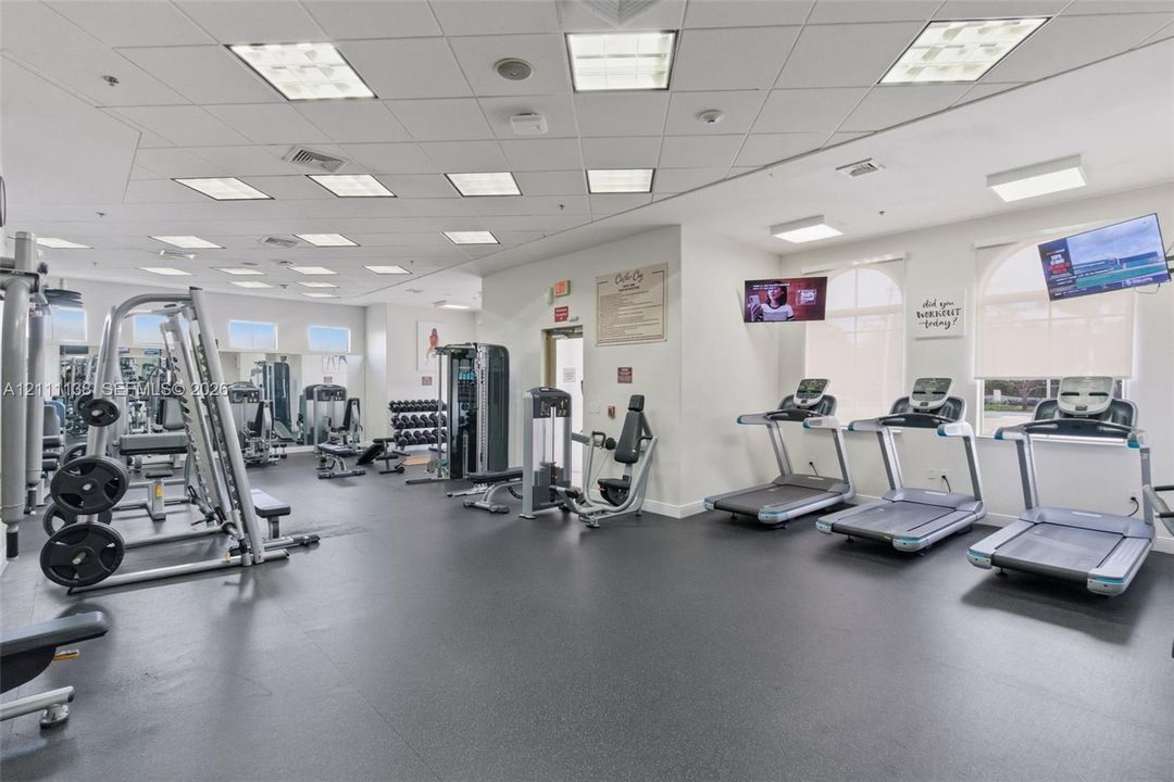 Fitness facility featuring rubberized flooring, recessed grid lighting, multiple treadmills, and wall-mounted televisions