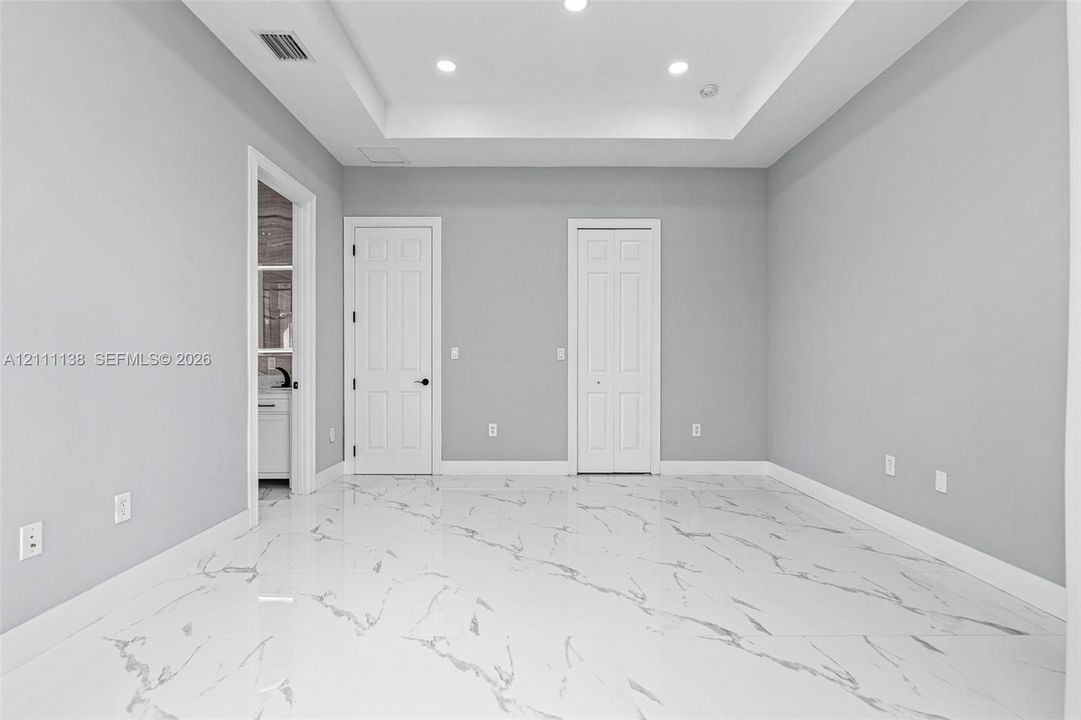 Interior space featuring a recessed tray ceiling, large-format stone-patterned tile flooring, and integrated recessed lighting