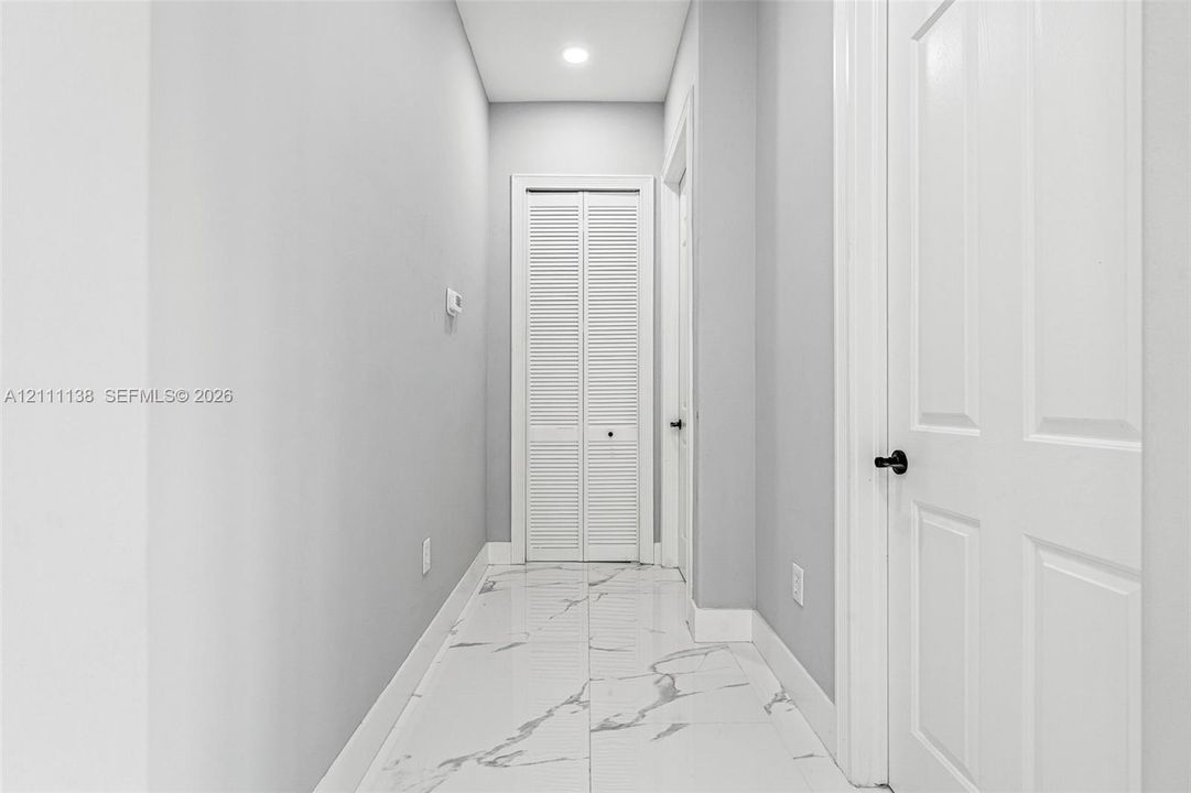 Hallway featuring polished tile flooring with a veined pattern, recessed ceiling lighting, and crisp white interior doors with matte black hardware