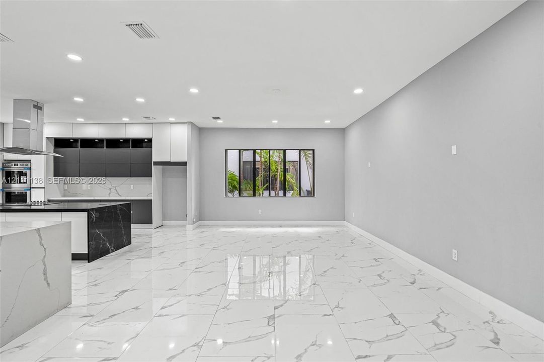 Open-concept interior featuring large-format polished stone-finish flooring, two-tone cabinetry with contrasting stone-finish countertops, stainless steel wall oven, and recessed lighting