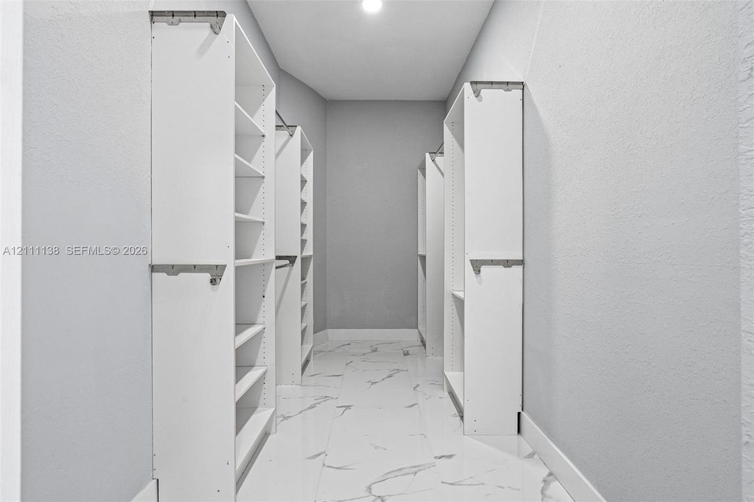 Walk-in closet featuring white built-in shelving, multiple hanging rods, and large-format tile flooring with a neutral vein pattern
