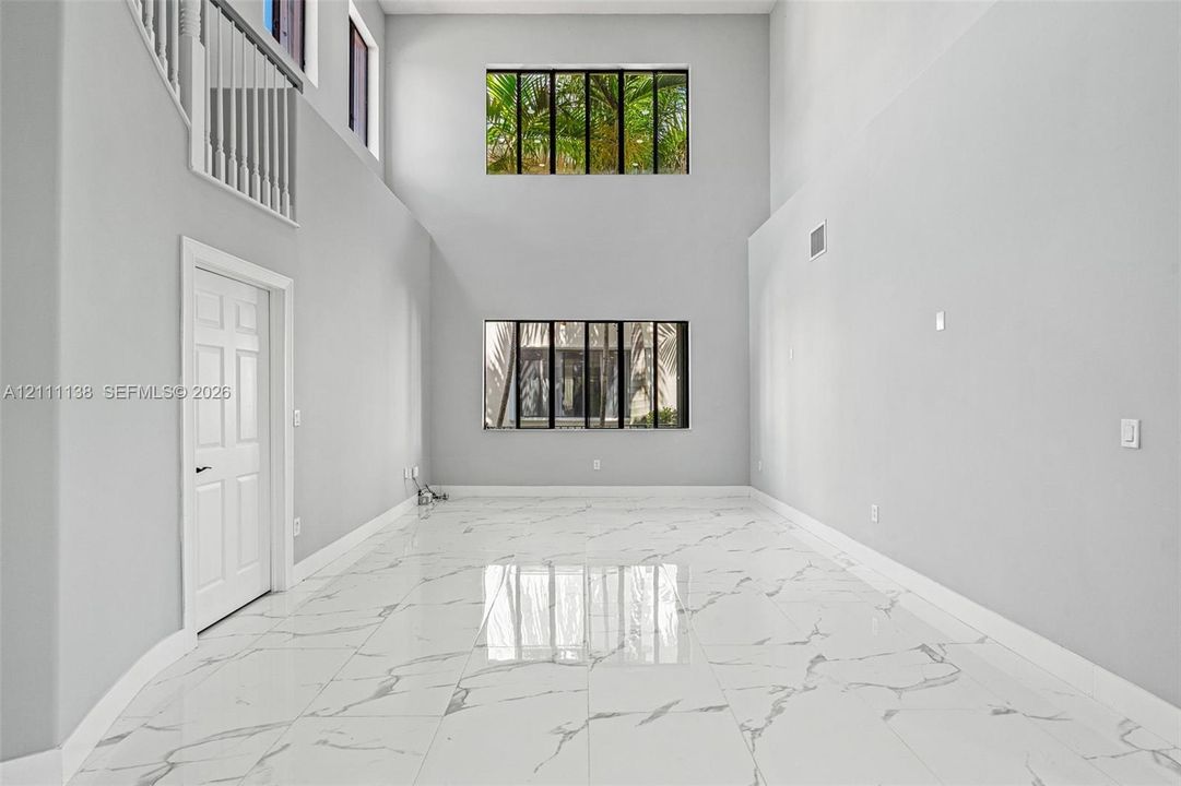 High-ceiling interior featuring polished tile flooring with marble-patterned finish, two tiers of large picture windows, and a white interior railing