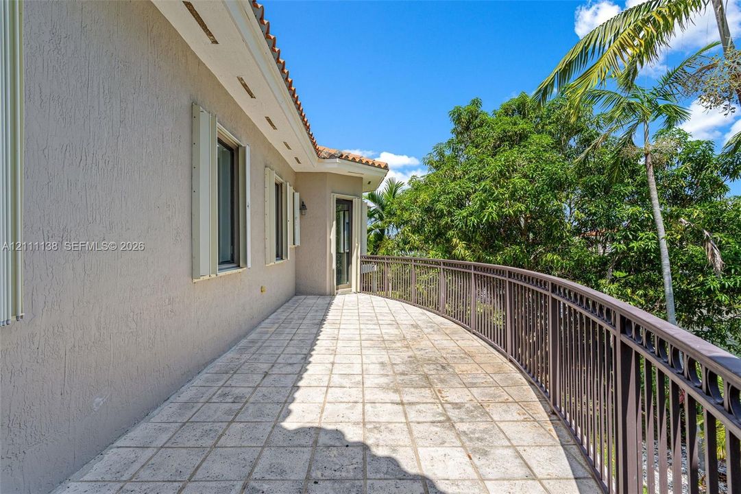 Curved exterior terrace featuring stone-finish tile flooring, a metal railing, and stucco wall construction