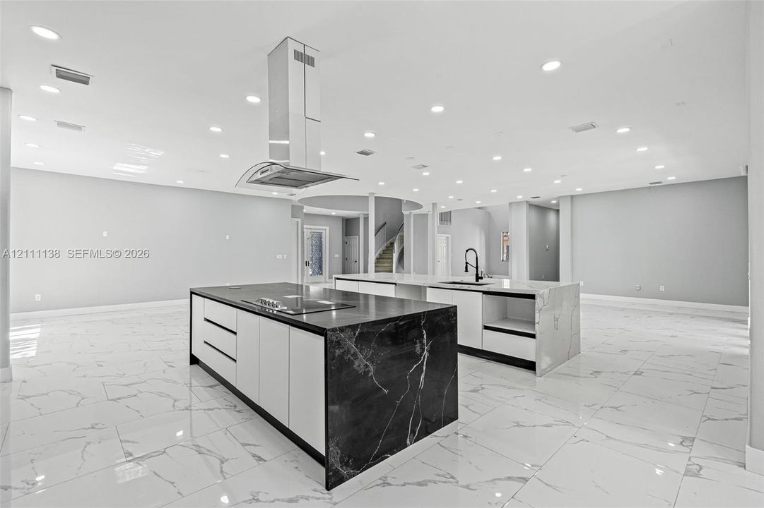 Dual kitchen islands featuring stone-finish waterfall countertops, flat-panel cabinetry, a stainless steel chimney-style range hood, and porcelain tile flooring throughout