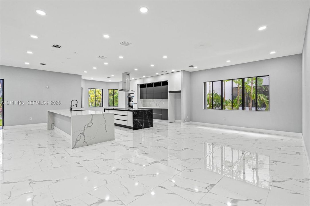 Open-concept kitchen featuring dual islands with veined stone-finish countertops, matte black plumbing fixtures, two-tone flat-panel cabinetry, and polished large-format tile flooring