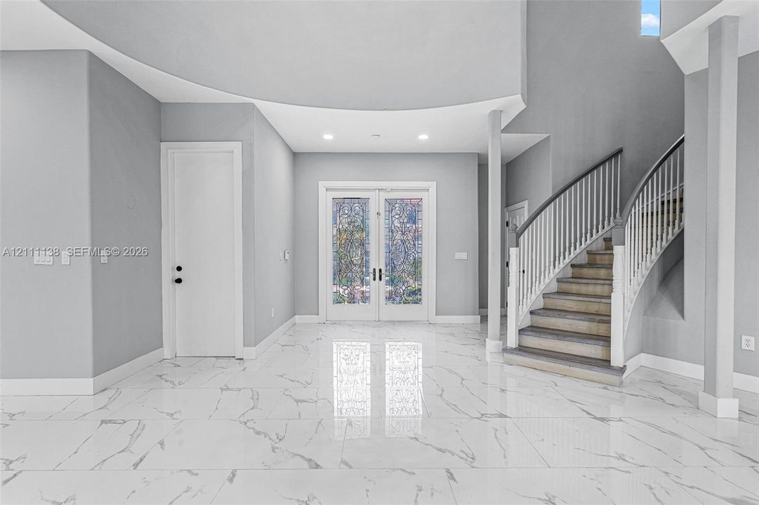 Foyer featuring large-format veined tile flooring, a curved staircase with white spindles, high ceilings with recessed lighting, and double-entry doors