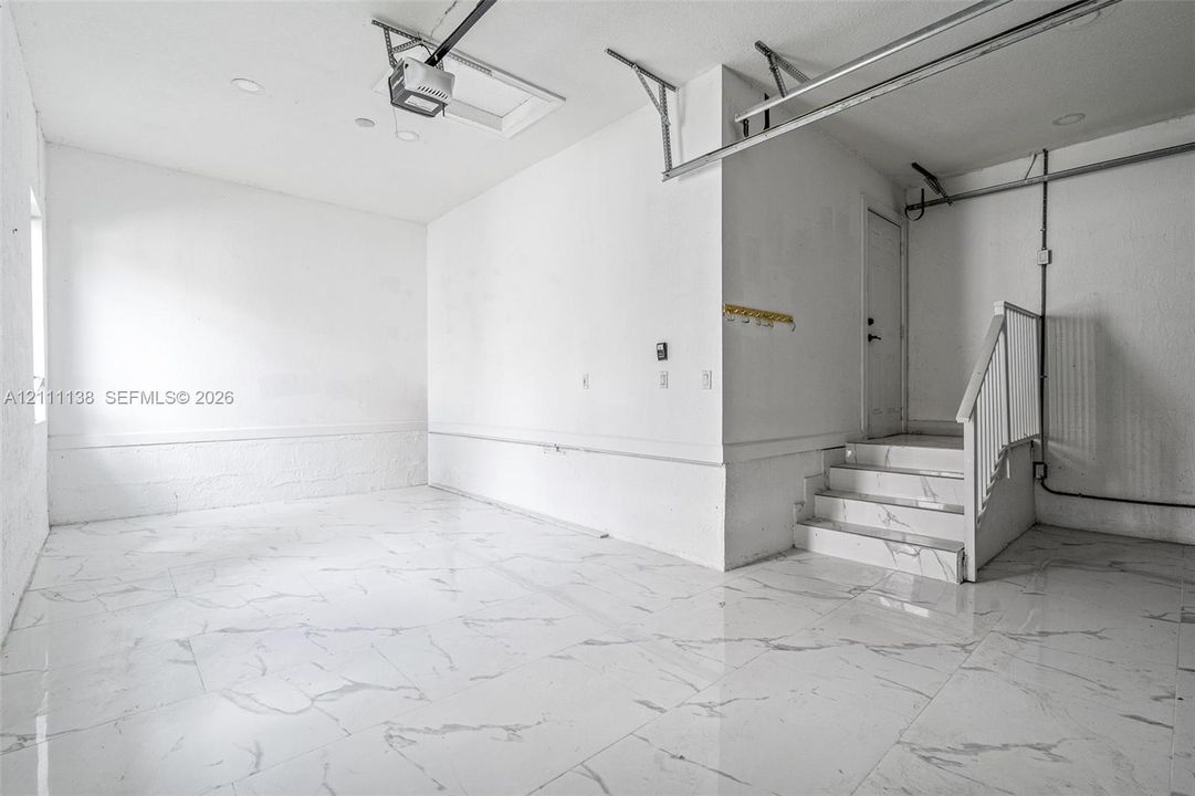 Finished garage space featuring large-format tile flooring, a staircase with matching tile risers and treads, recessed lighting, and white wall finishes