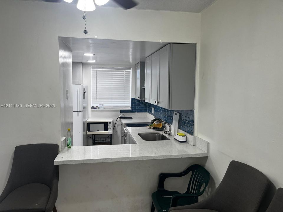 Kitchen featuring light-colored cabinetry, stone-finish countertops, a stainless steel undermount sink, blue tile backsplash, and a breakfast bar