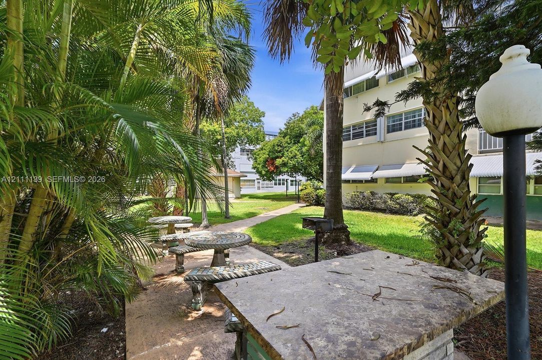 Common area featuring stone-finish picnic tables, a built-in outdoor grill, manicured lawn, and mature palm trees