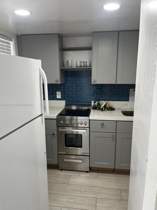 Kitchen featuring gray cabinetry, blue subway tile backsplash, light-toned stone-finish countertops, stainless steel range, and wood-finish flooring