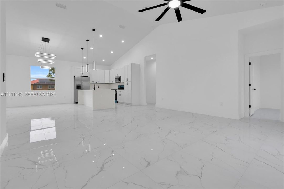 Open living area with cathedral ceiling, ceiling fan, and 32x32 polished Calacatta-style porcelain tile open to the kitchen.