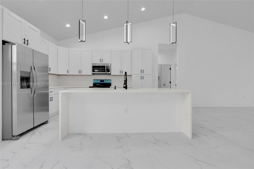 Large waterfall-edge quartz island with stainless steel refrigerator and full-height backsplash.