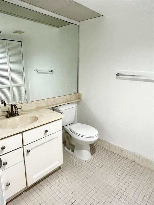 Bathroom featuring white cabinetry, a neutral-toned countertop with an integrated sink, full-width wall mirror, and tiled flooring
