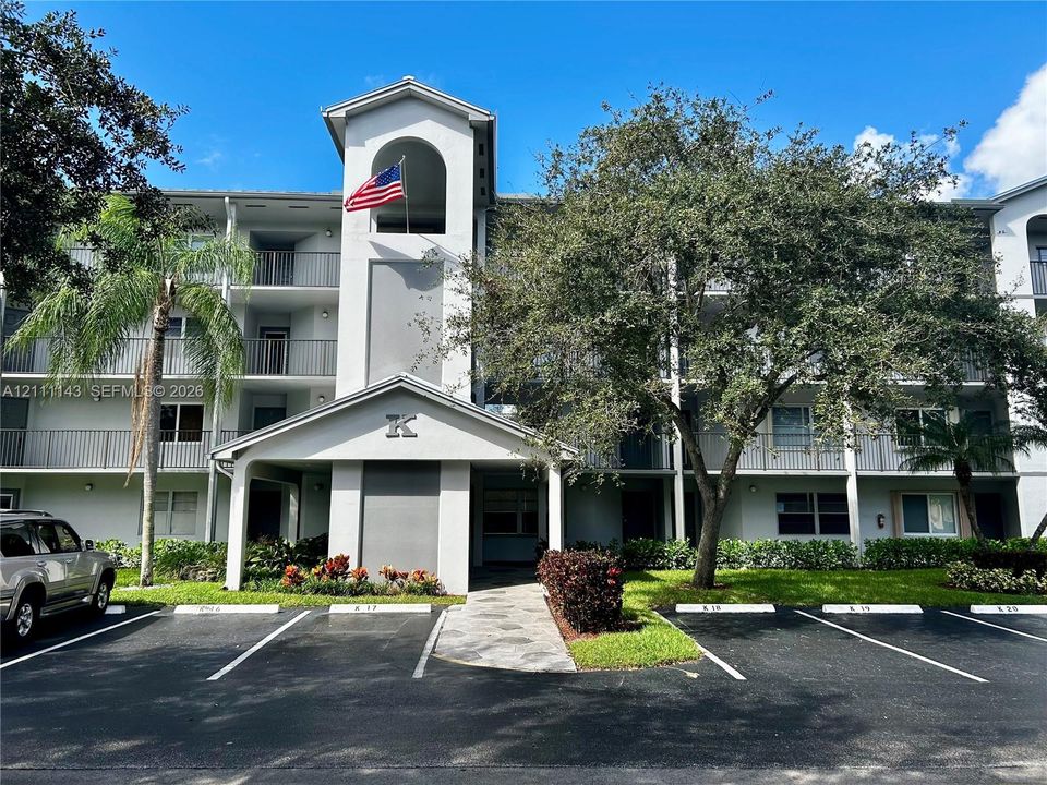 Multi-story exterior featuring a covered entryway, arched architectural detailing, private balconies with metal railings, and mature landscaping