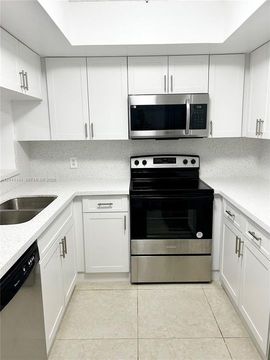 Kitchen featuring white shaker-style cabinetry, speckled solid surface countertops, stainless steel appliances, a double-basin undermount sink, and recessed ceiling lighting