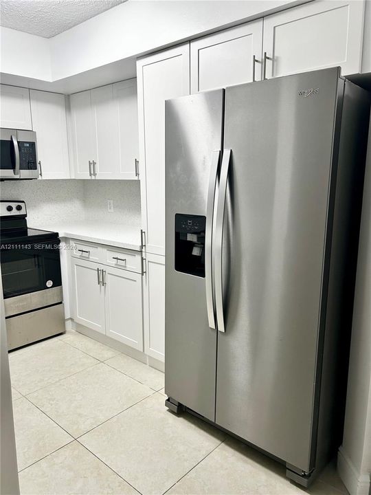 Kitchen featuring white shaker-style cabinetry, stainless steel appliances, solid surface countertops, and light-toned tile flooring