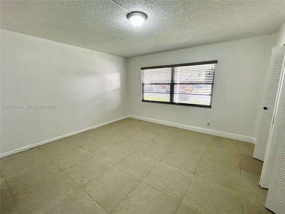 Neutral-toned tile flooring, white wall finishes, horizontal window blinds, and louvered closet doors