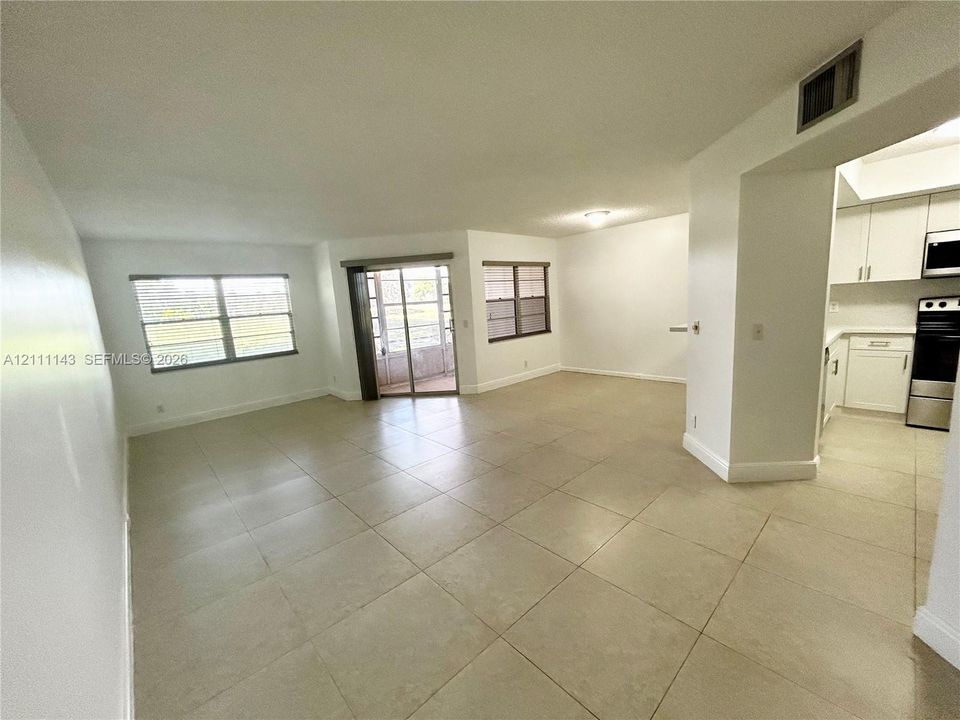 Open-concept floor plan with neutral ceramic tile flooring, sliding glass door, and large windows providing natural light