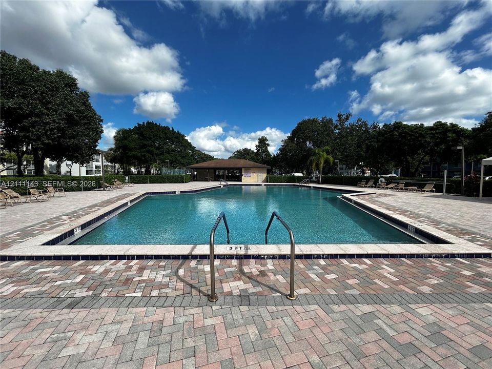 In-ground swimming pool featuring a brick paver deck, metal pool handrails, and a covered pavilion