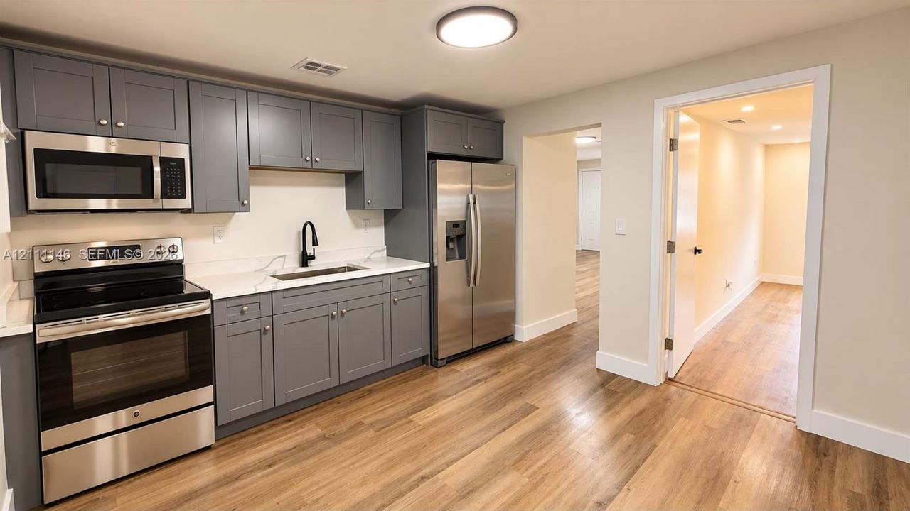 Kitchen featuring charcoal shaker cabinetry, solid-surface countertops, wood-finish flooring, and a stainless steel appliance suite including a French-door refrigerator and built-in microwave