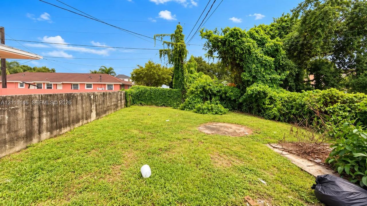Backyard featuring a concrete perimeter wall, lawn, and mature perimeter landscaping