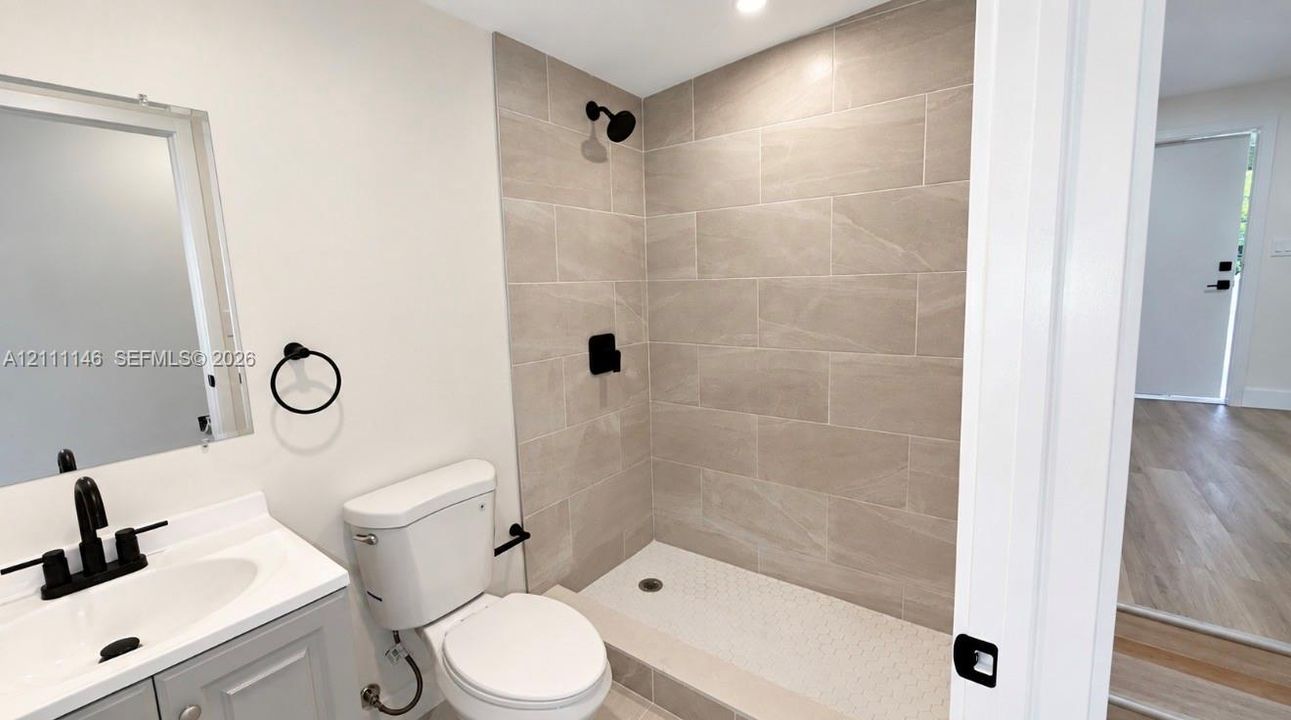 Bathroom featuring a walk-in shower with light-toned wall tile, a gray vanity with a white countertop, matte black fixtures, and a frameless mirror