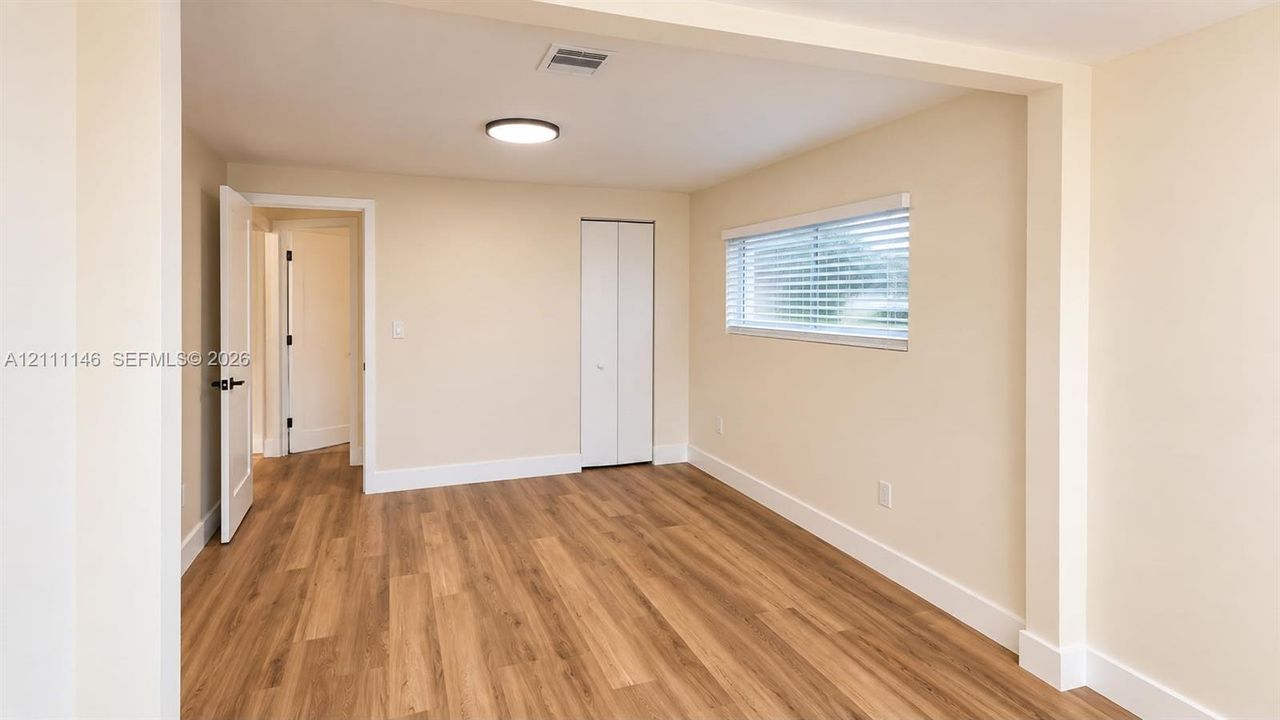 Neutral-toned interior featuring wood-finish flooring, a horizontal window with adjustable blinds, a ceiling-mounted light fixture, and a reach-in closet with bi-fold doors