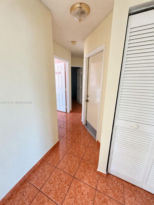 Hallway featuring tile flooring, white louvered-door closets, and flush-mount ceiling lighting