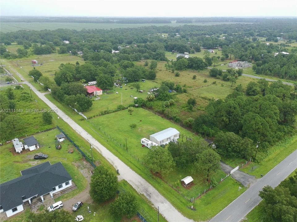 Aerial perspective of expansive acreage featuring mature trees, open grassy areas, fenced perimeter, and rural road frontage