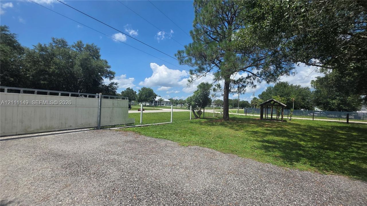 Gravel driveway, perimeter fencing, mature trees, open grassy area, and detached wooden structure