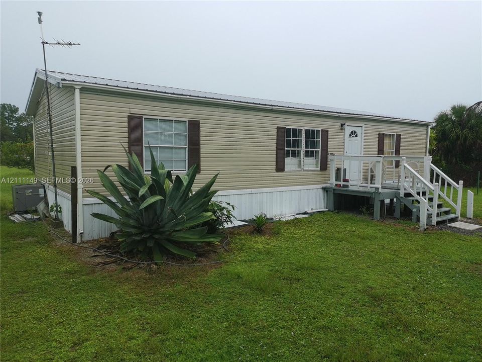 Exterior featuring light-toned horizontal siding, dark-toned shutters, a metal roof, and an elevated front deck with stairs and railings