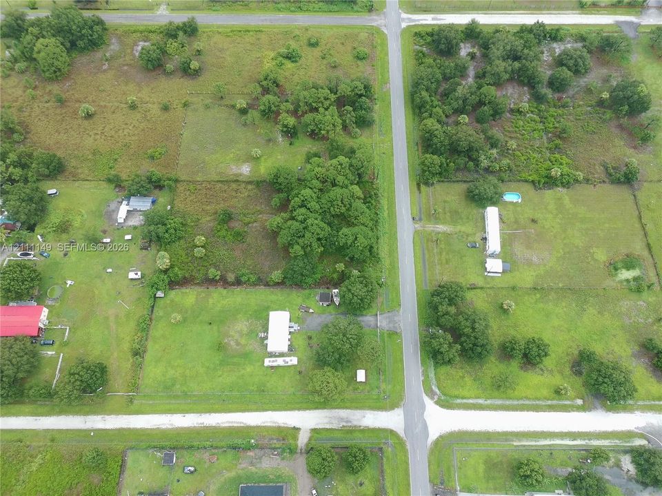 Aerial perspective of expansive acreage featuring mature trees, cleared open space, and direct paved road frontage