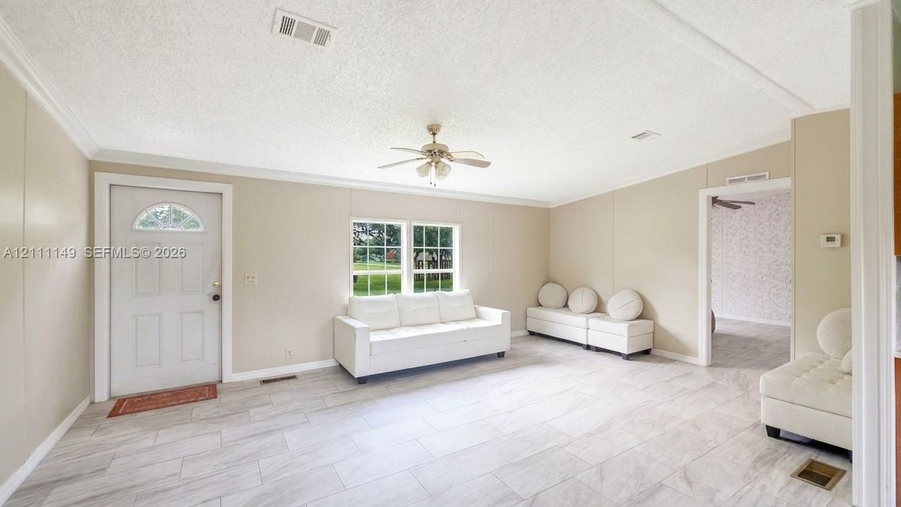 Neutral-toned interior featuring large-format tile flooring, a centered ceiling fan with integrated lighting, a multi-pane window, and an exterior door with a semi-circular transom glass insert