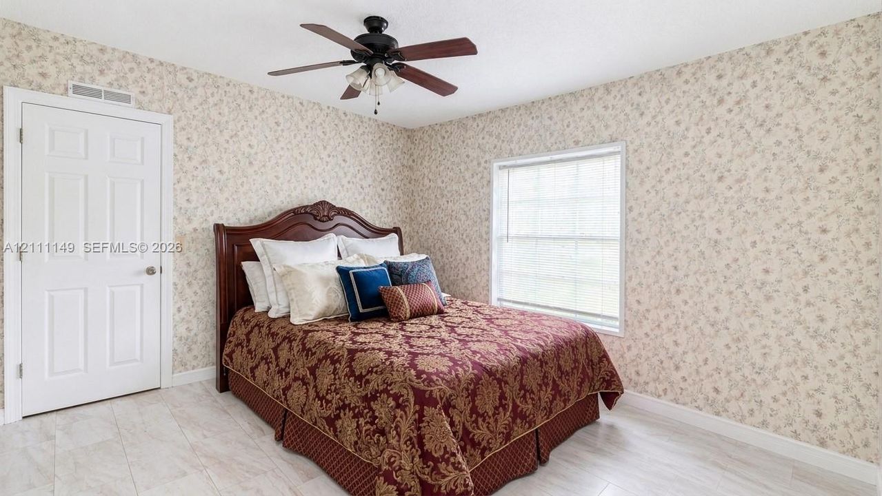 Room featuring white-toned tile flooring, floral patterned wallpaper, a single window, and a multi-blade ceiling fan with integrated lighting