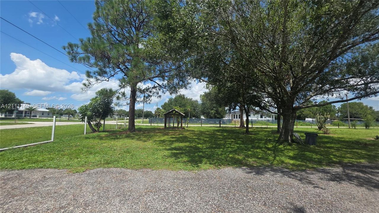 Expansive lot featuring mature shade trees, a gravel surface, and perimeter fencing