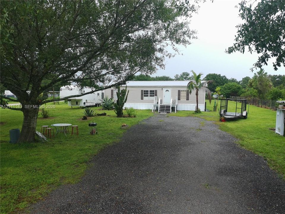 Exterior facade featuring a metal roof, shuttered windows, and a gravel driveway situated on a lot with mature trees and vegetation