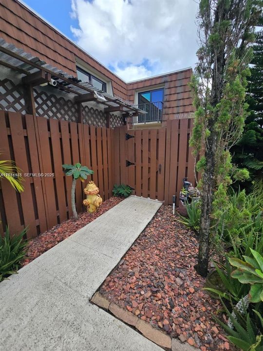 Concrete walkway leading to a private entrance, enclosed by a wood-slat privacy fence with integrated lattice detailing