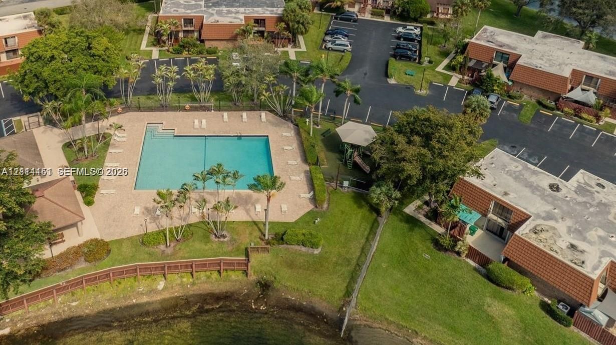 Aerial perspective of common area amenities including a rectangular swimming pool with paved decking, lush landscaping, mature trees, and designated surface parking