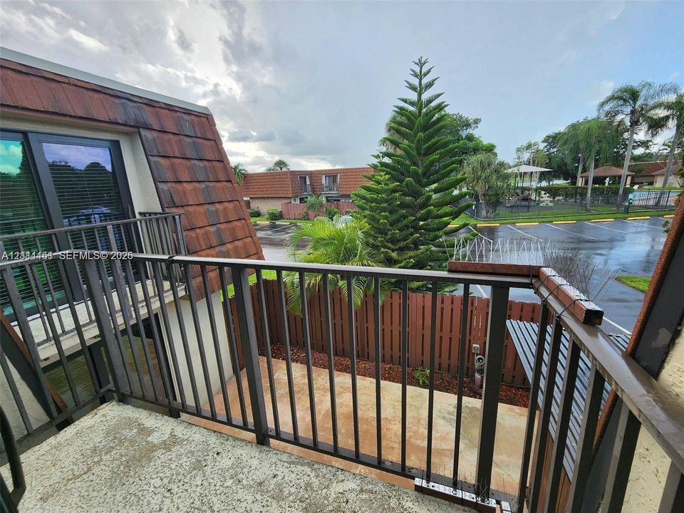 Private balcony featuring metal railings, textured concrete flooring, and an architectural mansard roofline