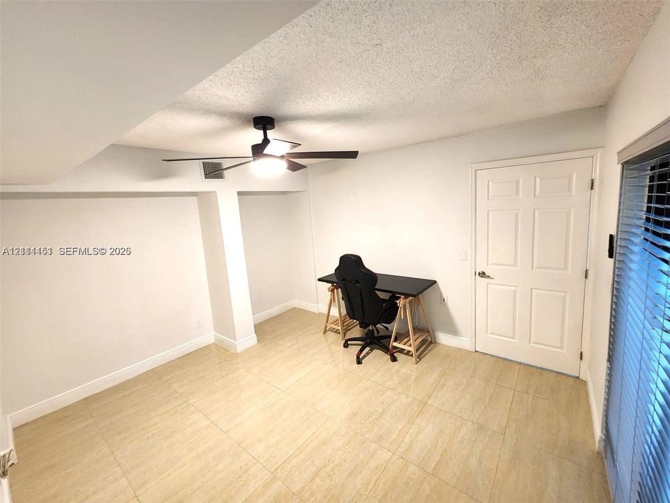 Neutral-toned tile flooring, recessed ceiling finish, matte black ceiling fan with integrated lighting, and a six-panel interior door