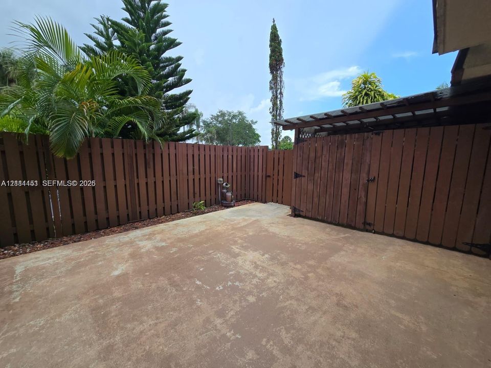 Private patio area enclosed by wood fencing, featuring a concrete surface and a covered storage structure
