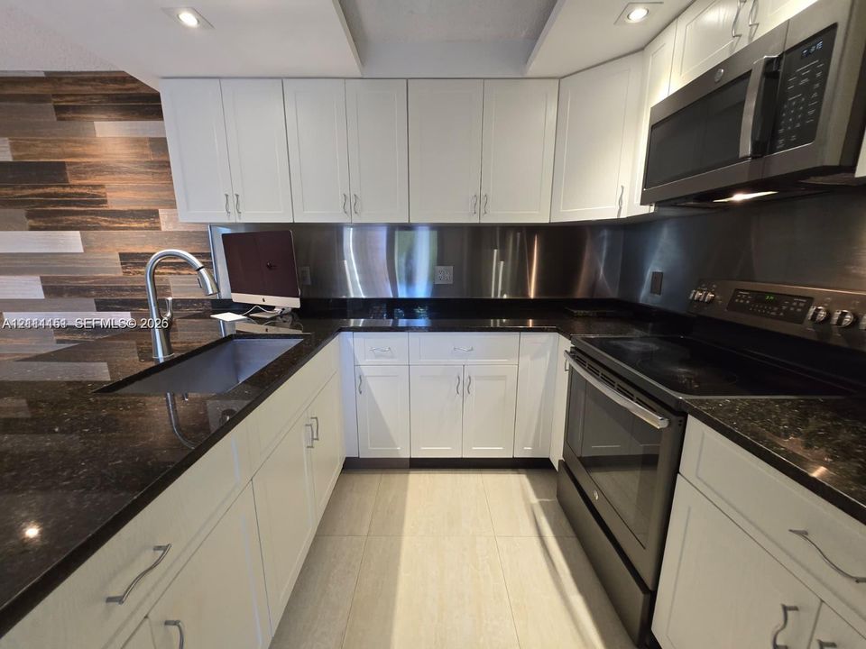 Kitchen featuring white shaker-style cabinetry, dark stone countertops, stainless steel backsplash, integrated appliances, and wood-finish accent wall paneling