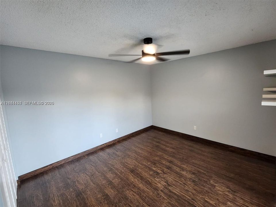 Room featuring wood-finish flooring, a ceiling fan with integrated lighting, and built-in wall shelving
