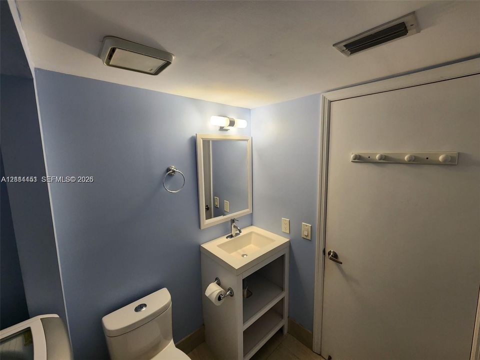 Bathroom featuring a white vanity with an integrated sink, wall-mounted light fixture, rectangular mirror, and dual-flush toilet