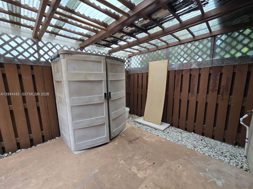 Enclosed patio area featuring wood privacy fencing, decorative lattice paneling, a translucent corrugated roof, and a gravel stone border